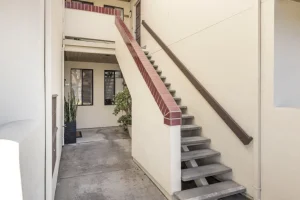 Concrete staircase with red brick trim leading to an upper apartment entrance in a beige residential building.