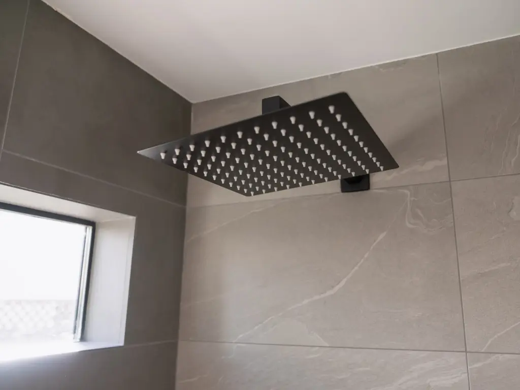 Square black showerhead installed on a gray tile wall near a window
