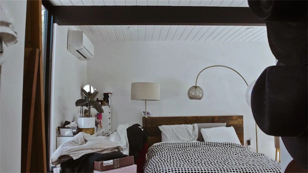 Cozy bedroom with wooden bed frame, polka-dot bedding, arched floor lamp, and cluttered nightstand against white walls.