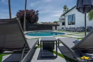 Modern backyard with lounge chairs facing a round swimming pool beside a white house with patio seating.