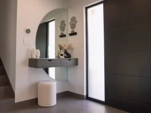Modern entryway with round wall mirror, floating console table, decorative accents, and frosted glass front door
