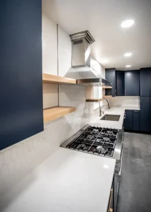 Close-up view of a modern kitchen cooktop with stainless steel range hood, open wood shelves, and white backsplash