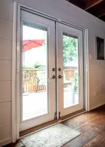 White French doors opening to a wooden deck with patio furniture and a red umbrella.